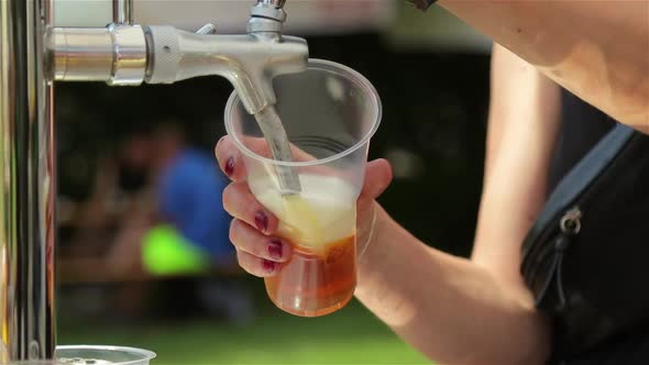 the girl  pours beer in a plastic glass. close up. street food festival