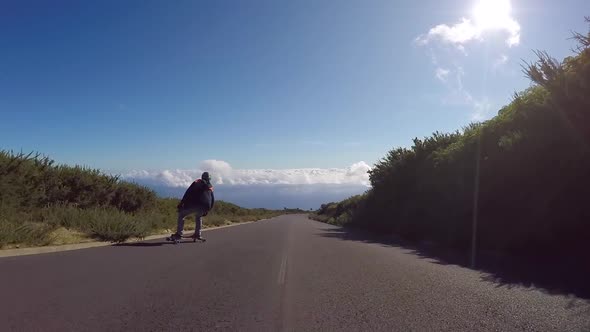 POV of young men longboard skateboarding downhill on a rural country road alt
