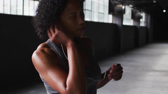 Portrait of african american woman standing in an empty building putting earphones in alt