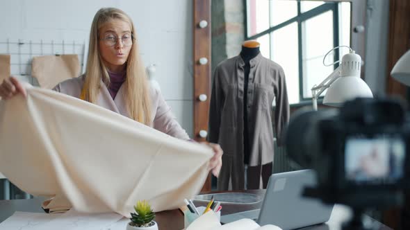 Young Woman Dressmaker Recording Video for Internet Vlog Talking and Showing Sketches Using Camera alt