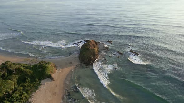 Cinematic aerial orbit around a giant rock on the tip of narrow peninsula. Playa Ventanas and playa alt