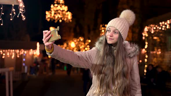 Beautiful teenager with long hair taking a selfie at Christmas market. alt