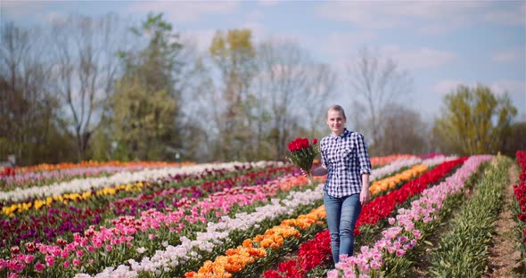 Woman Holding Tulips Bouquet in Hands While Walking on Tulips Field alt