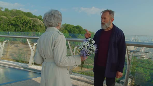 Elderly Bearded Man and Woman with Flowers Quarreling Outdoors alt