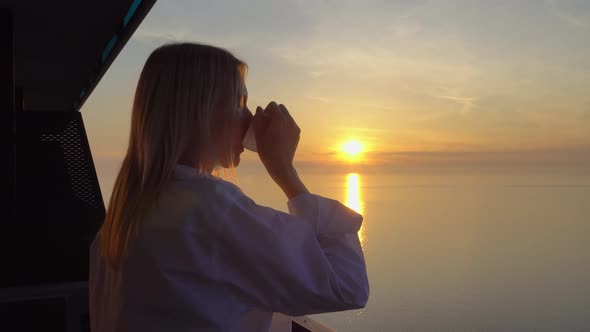 a woman admires the sunset over the sea, and drinks coffee on a high floor. alt