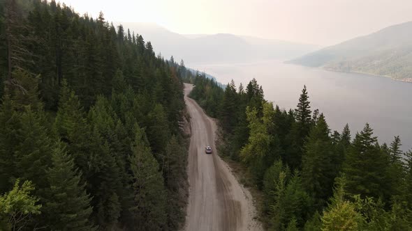 Silver car driving along a dusty forest service road during wildfire season with Adams Lake in the b alt
