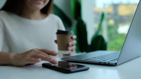 a woman touching and scrolling on smart phone screen while working on laptop computer