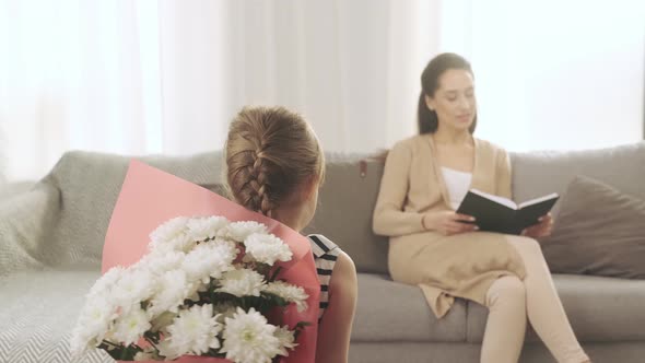 Daughter is Hiding a Bouquet of White Flowers for Her Beautiful Mother Behind Her Back While She is alt