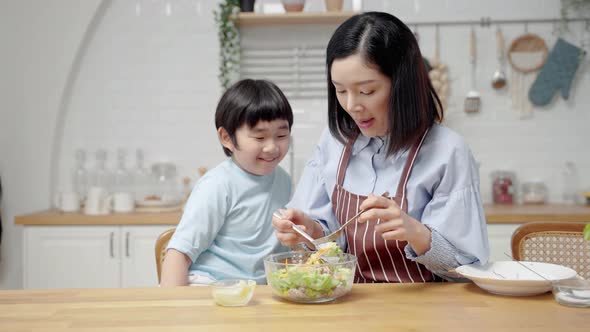 Asian happy family cooking in kitchen room at house.Mother is feeding her son salad
