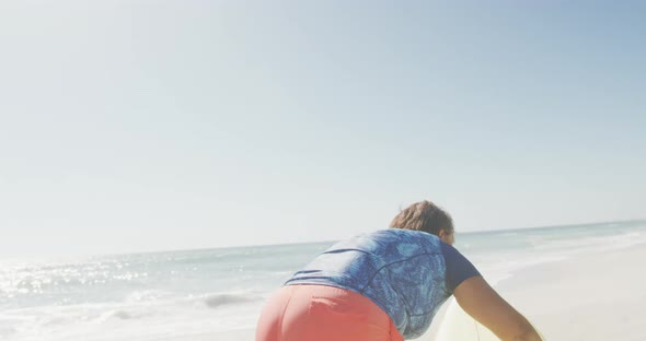 Happy senior african american woman carrying surfboard on sunny beach alt