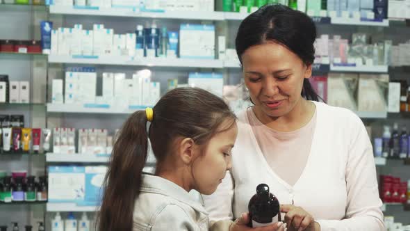 A Smiling Woman Chooses with Her Daughter Something in the Pharmacy alt