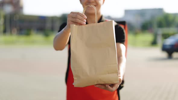Happy Delivery Worker Holding Packet With Food Looking at the Camera and Smiling