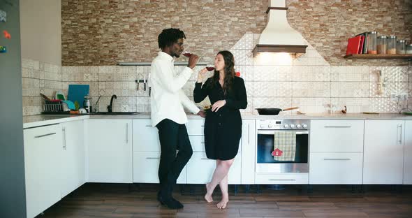 Young Couple Talk and Drink with Glasses of Wine Stand in Kitchen alt