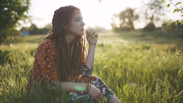 Beautiful Hippie Woman with Dreadlocks in Green Grass at Sunset Having Good Time Outdoors alt