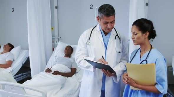 Front view of multi-ethnic doctors discussing over clipboard in ward at hospital alt