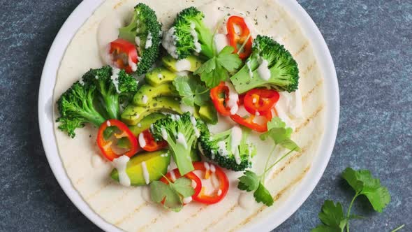 Vegan Tortilla with Broccoli Avocado and Cream Cheese Revolving on Blue Background alt