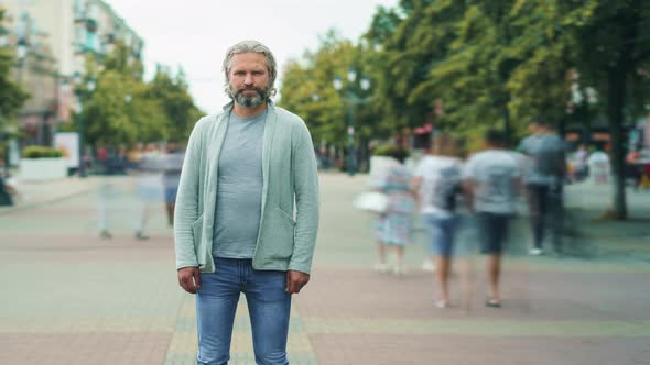 Zoomout Time Lapse of Grayhaired Man in Casual Clothing Standing Outdoors in Busy Street alt