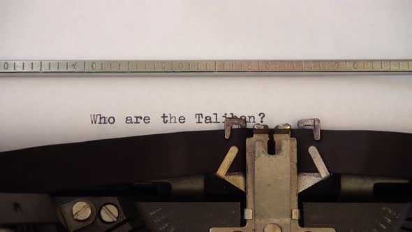 Typing phrase Who are the Taliban ? on retro typewriter. Close up. alt