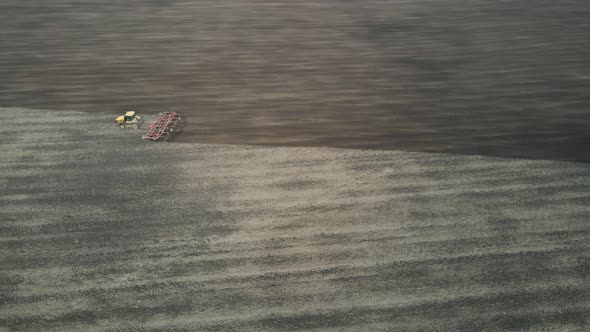 Aerial view of a modern yellow tractor plowing dry agricultural field, preparing land for sowing alt