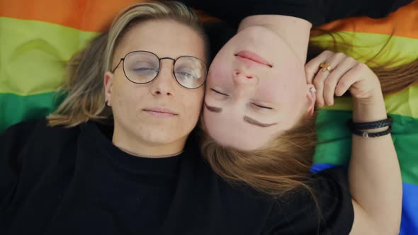 Pretty LGBT Couple Lying on Rainbow Flag and Looking at you alt