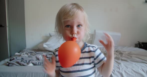 Cute Happy Baby Girl Blowing Orange Balloon Playing and Smiling alt