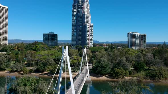 A pedestrian bridge leading into a park near a large city alt
