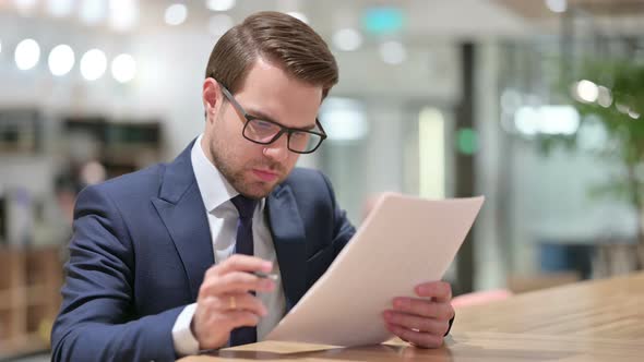 Young Businessman Reacting To Loss on Documents at Work  alt