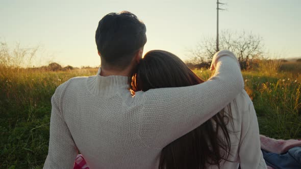 Couple watches the sunset sitting on the picnic tablecloth alt