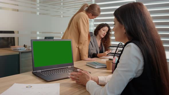 Office workers engaged in a project one watching a green screen laptop. alt