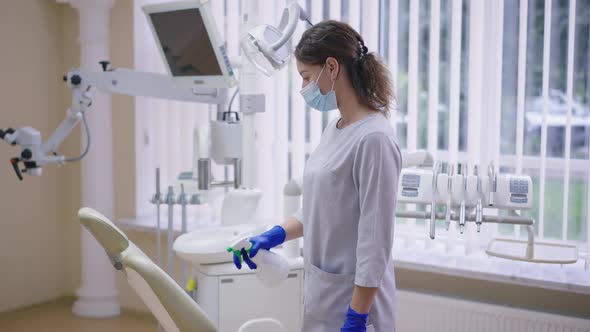 Female Dentist Assistant Spraying Disinfectant Cleaning Chair in Hospital Indoors alt