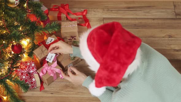 Writing Greeting Card for Christmas Presents Female Red Hat Under Fir Tree Gifts alt