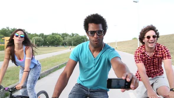 Group of friends having fun cycling and taking selfies with phone alt