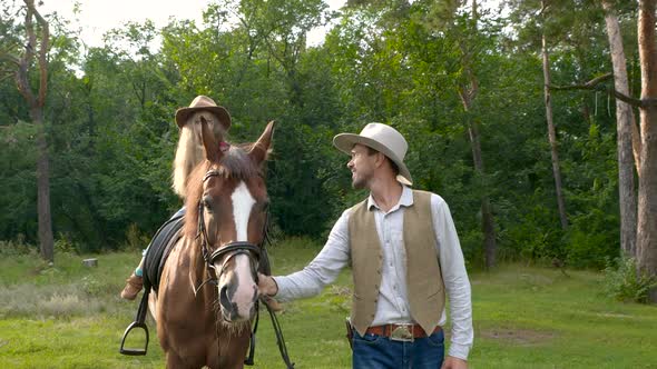 A Young Cowboy is Leading a Horse on Which His Daughter is Sitting alt