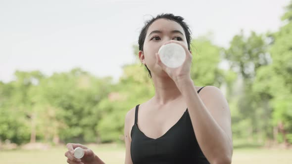 asian woman drinking from a bottle after exercising in the garden, healthy concept