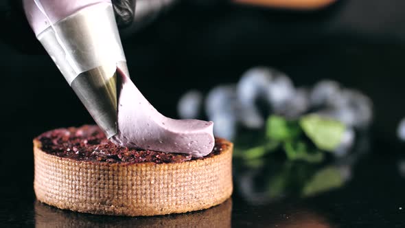 Pastry Chef Decorates Biscuit with Purple Cream From Pastry Bag, Close-up. alt