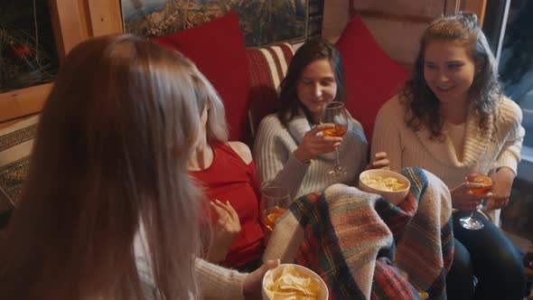 Excited Young Women Spending Winter Holidays in the Cozy Home Drinking Mulled Wine and Having Snacks alt