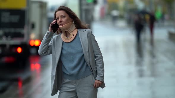 Adult Woman Is Talking By Cell Phone, Strolling in City, Lady Is Wearing Cervical Collar for Curing alt