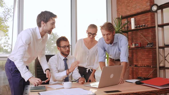 Three Succesful Businessmen and Businesswoman Discussing New Project Standing Around Table with