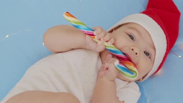 Smiling Funny Newborn Baby in Santa Claus Hat Red Bodysuit Play on White Soft Bed Lick Sweet alt