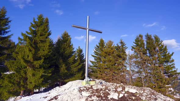 Christian iron cross on a rock. Blue sky with small clouds.Trees in the background. Timelapse 4K
