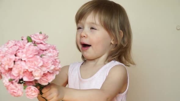Little Girl Holds Bouquet Pink Carnations Looks at Camera Smiles and Smells Flowers