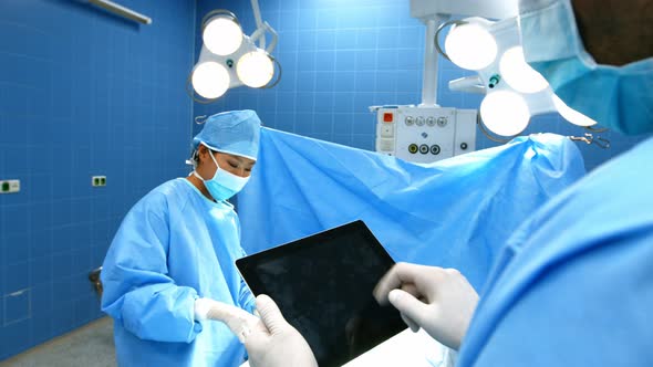 Surgeon using digital tablet while coworker operating patient in operation room alt