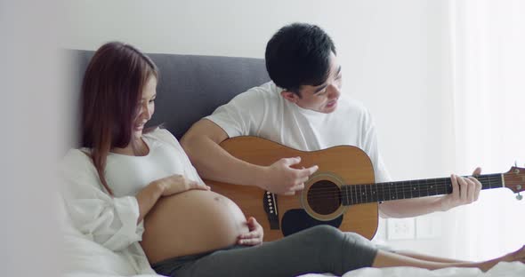 Happy Asian husband and pregnant wife spend time together in the bedroom.