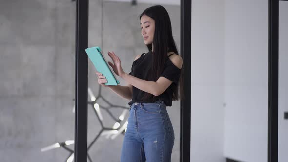 Confident Young Asian Businesswoman Scrolling Tablet Surfing Internet Standing in Luxurious Glass alt