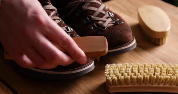 Man's hand clean suede shoes, boots with a brush on wooden background. alt