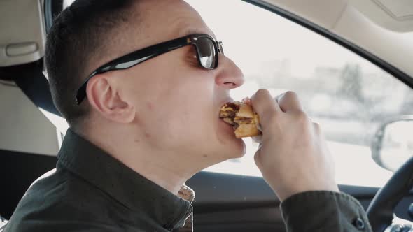 Man Eating a Burger at the Wheel of a Car