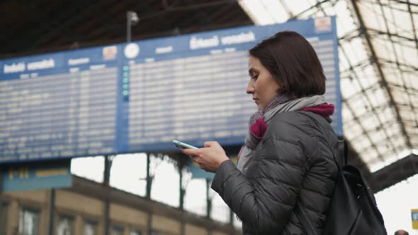 Нoung Woman is Using a Smartphone While Waiting for a Train As Arrival alt
