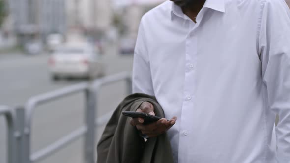 African Entrepreneur Scrolling on Smartphone while Waiting on Street alt