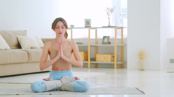 Relaxed woman in sportswear is meditating in lotus position sitting on yoga mat alt