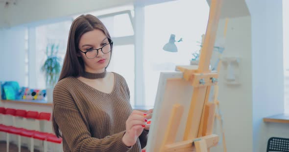 Artist Works at the Easel in the Studio. Girl Paints a Picture on Canvas. Side View alt